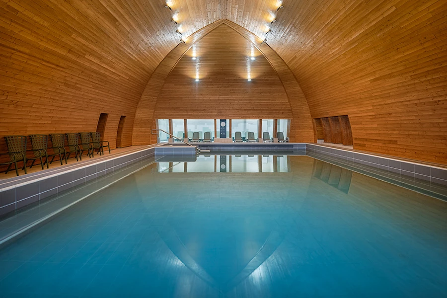 Indoor swimming pool with elegant wooden vaulted ceiling and lounge chairs