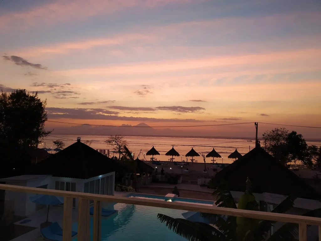 Sunset over a tropical beach with thatched huts and a pool
