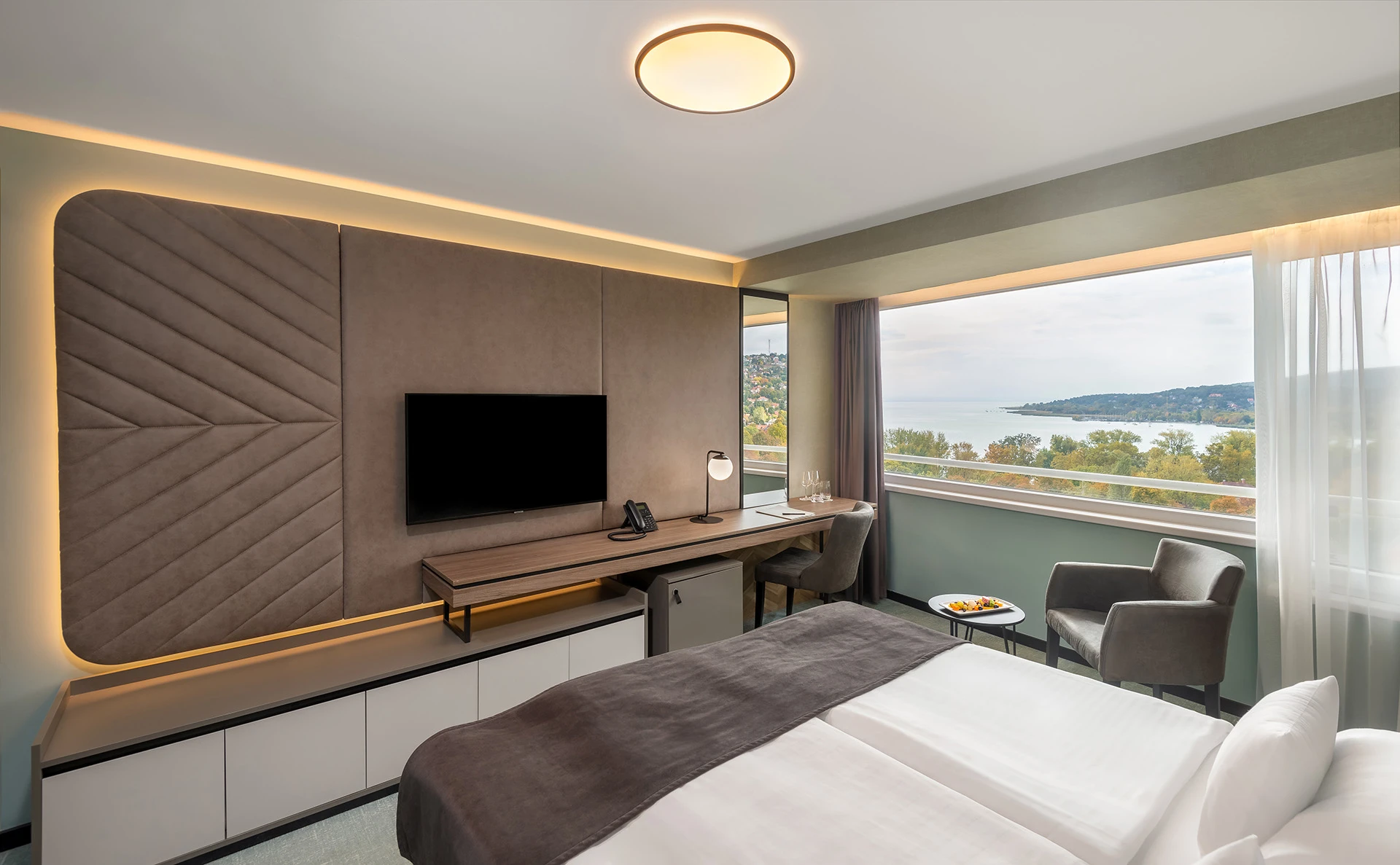 Spacious hotel room with panoramic window view and balanced interior composition.
