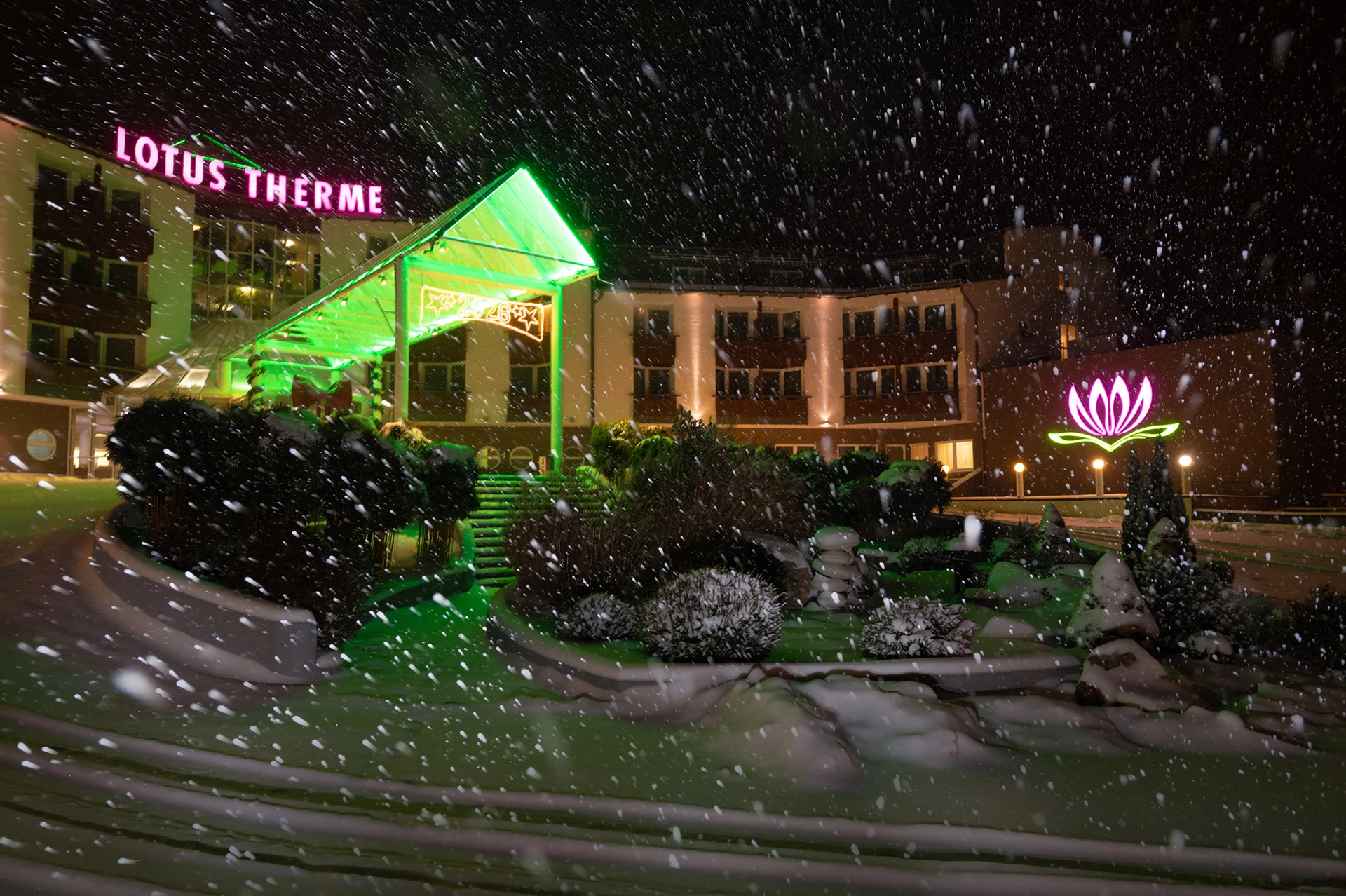 Lotus Therme Hotel & Spa entrance at night during heavy snowfall with neon lotus sign and illuminated facade