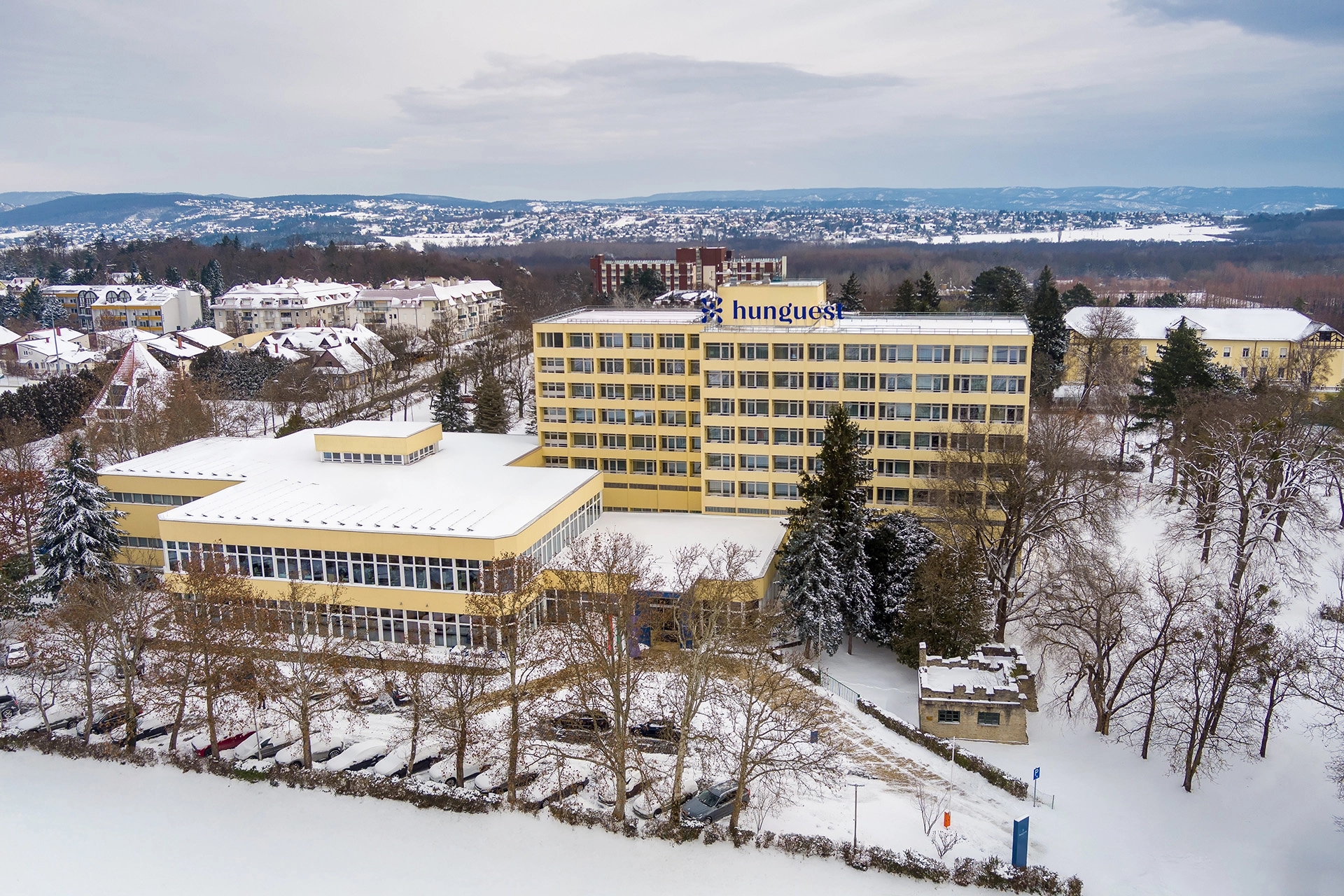 Aerial view of Hunguest hotel building in winter surrounded by snow-covered trees, streets and residential neighborhood