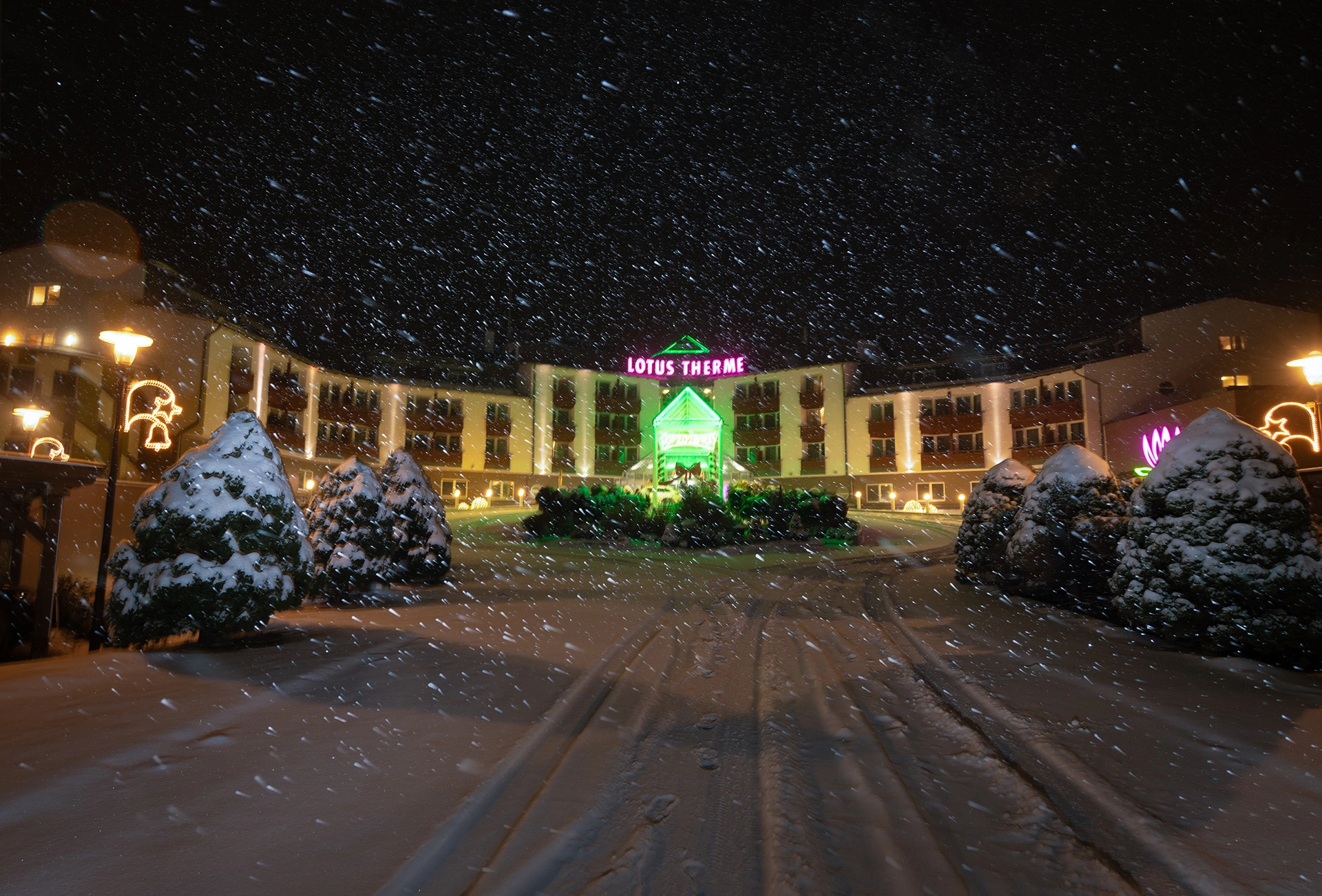Lotus Therme Hotel & Spa entrance at night during heavy snowfall with neon lights and illuminated facade