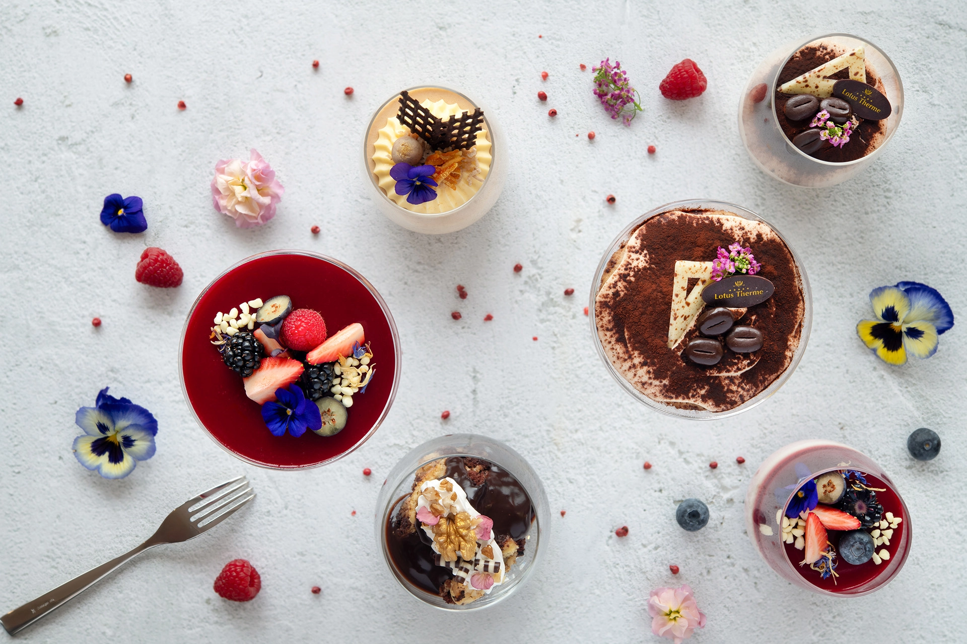 Flat lay of assorted desserts with berries, edible flowers, and chocolate details