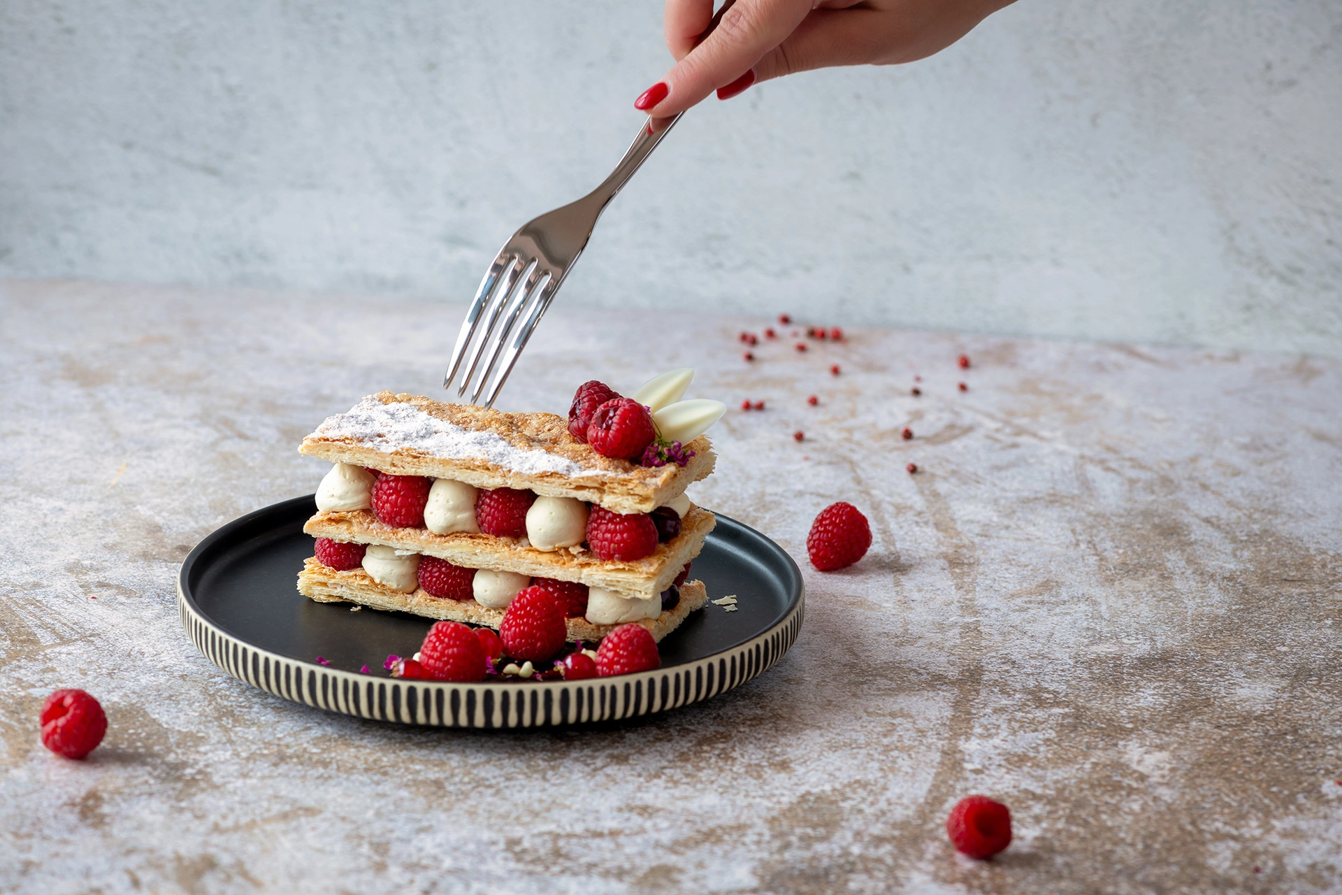 Fork cutting layered raspberry dessert with cream on black plate