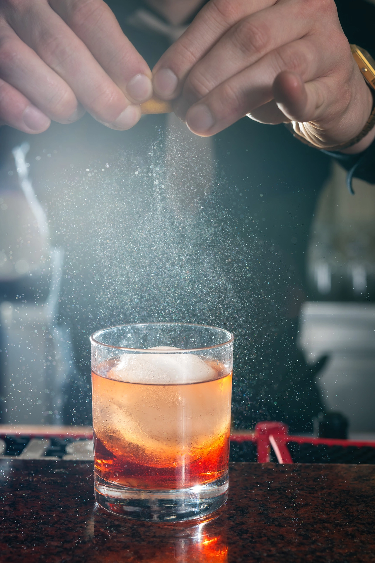 Bartender sprinkling sugar over cocktail with ice cube in glass
