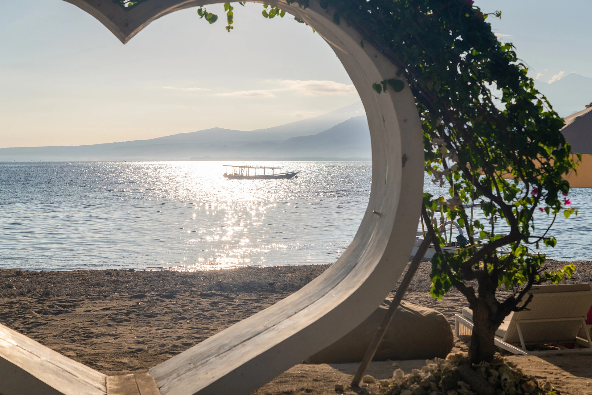Ocean view framed by a heart-shaped beachfront structure on Gili Air at sunrise.