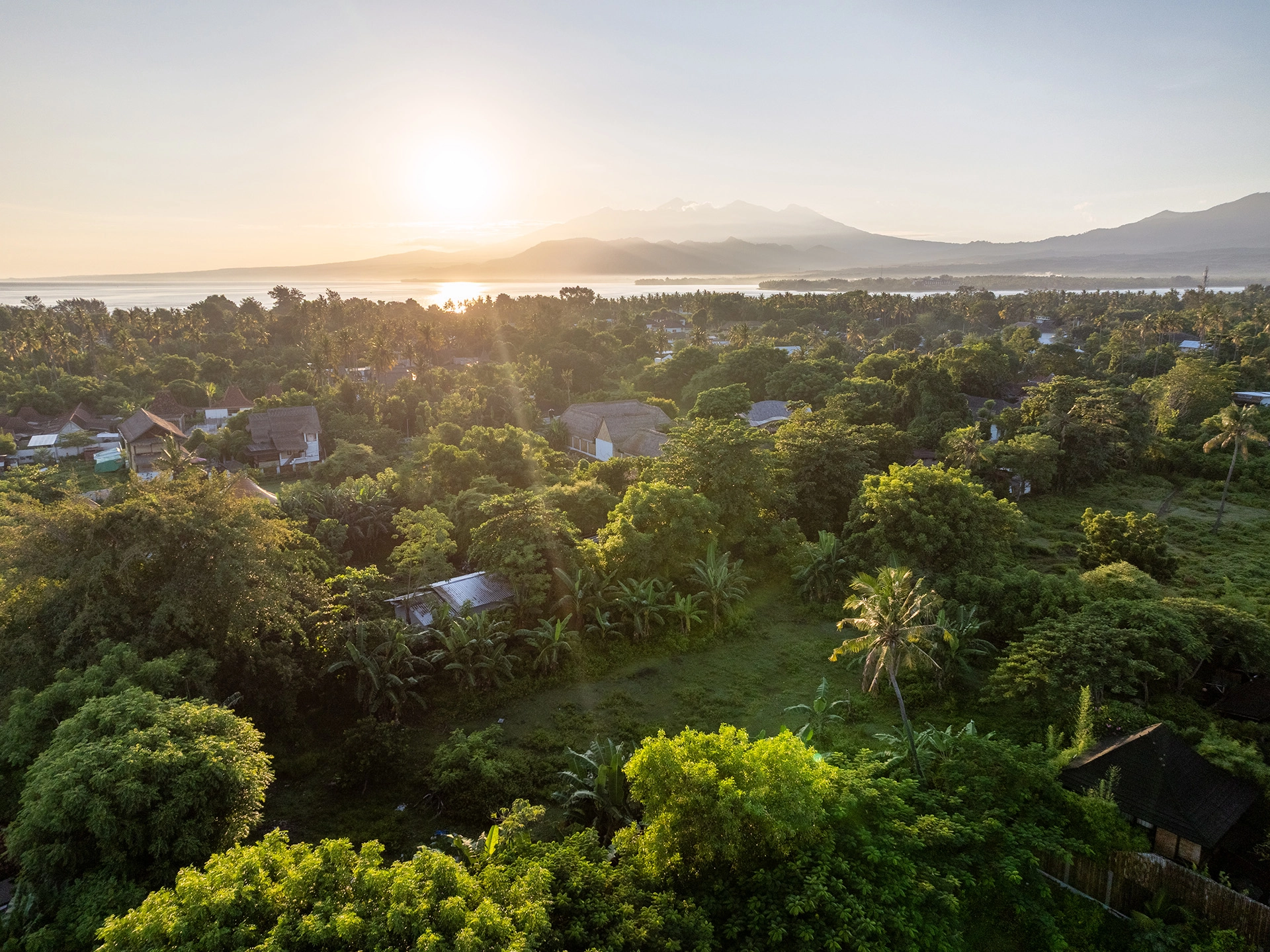 Sunrise view across Gili Air with tropical vegetation and Mount Agung visible in the distance.